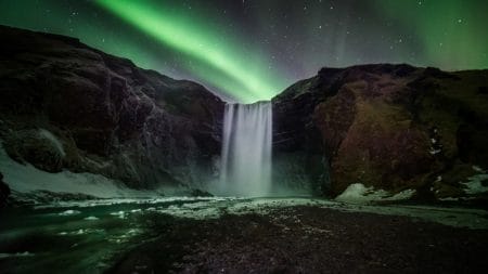 Aurora Borealis at a Frozen Waterfall: The Northern Lights cast a colorful glow over Skogafoss waterfall in Iceland. The aurora's lights reflect off the ice, creating a magical scene that combines natural beauty and winter wonder.