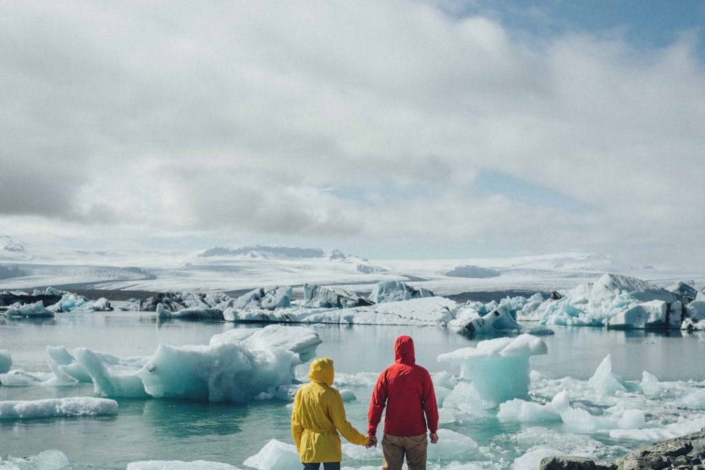 two people standing in front of Jokulsarlon glacier lagoon wearing yellow and red jackets