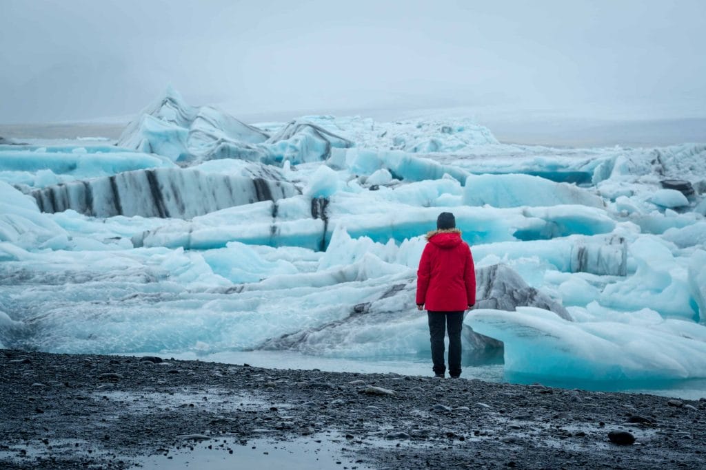 woman in red coat next to Jokulsarlon glacier lagoon in south Iceland