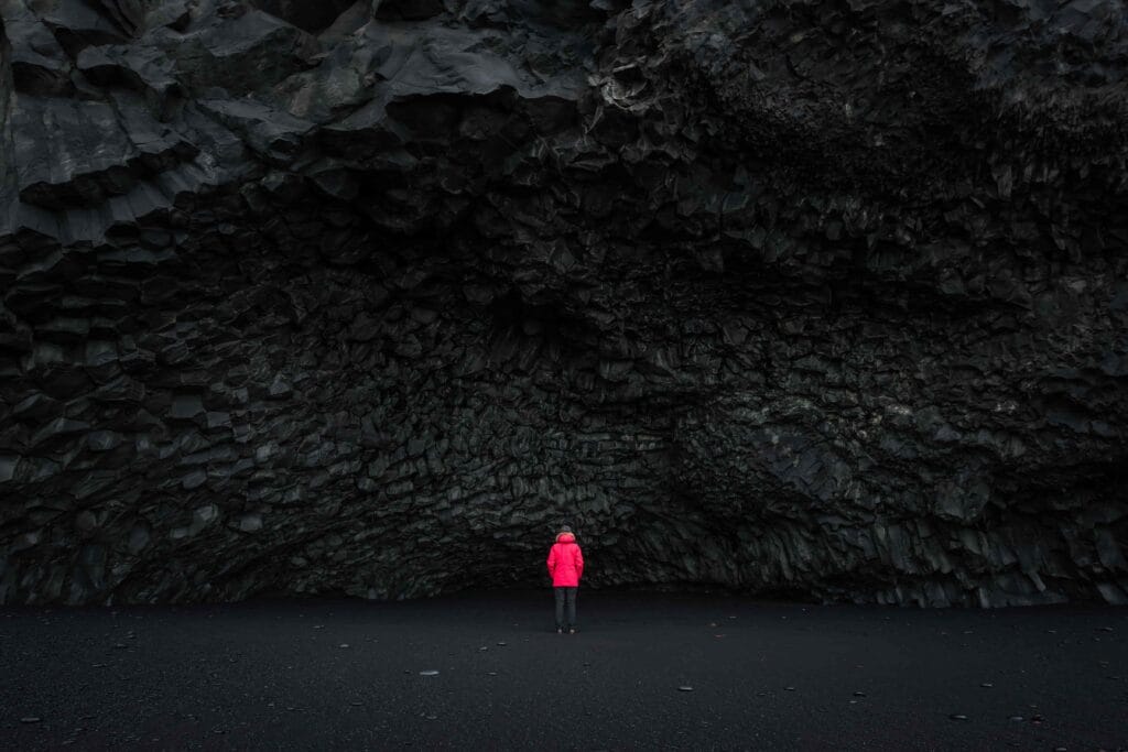 Black Sand Beach Tour, woman in red coat next to the cave at Reynisfjara black sand beach in south Iceland, Hálsanefshellir cave on Reynisfjara black sand beach, Iceland solo travel, Iceland female solo travel