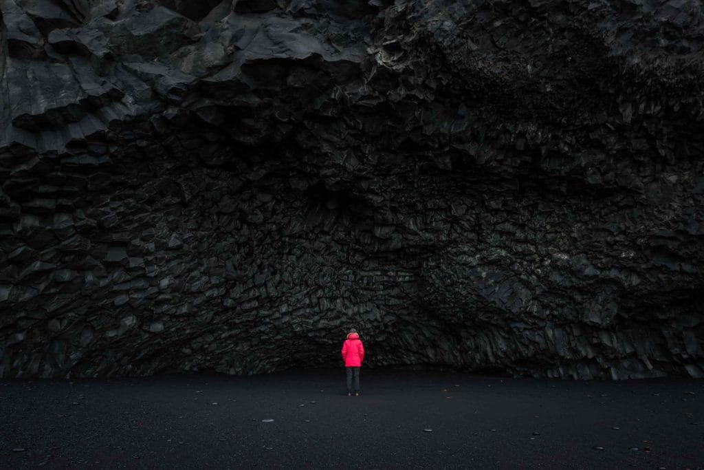 Black Sand Beach Tour, woman in red coat next to the cave at Reynisfjara black sand beach in south Iceland, Hálsanefshellir cave on Reynisfjara black sand beach