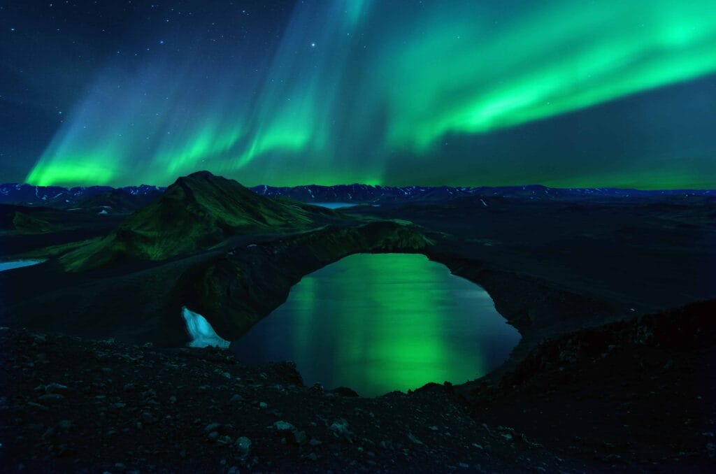 Northern Lights Reflecting on a Lake: The ethereal glow of the Aurora Borealis reflects on the surface of a calm lake in Iceland. The bright colors swirl in the sky, casting a mesmerizing light across the water and surrounding snowy terrain.