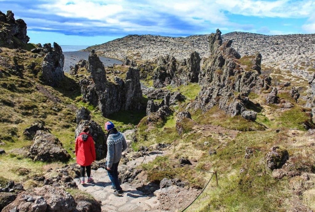 two people walking through lava fields on the way to Djúpalónssandur black sand beach in Snæfellsnes peninsula