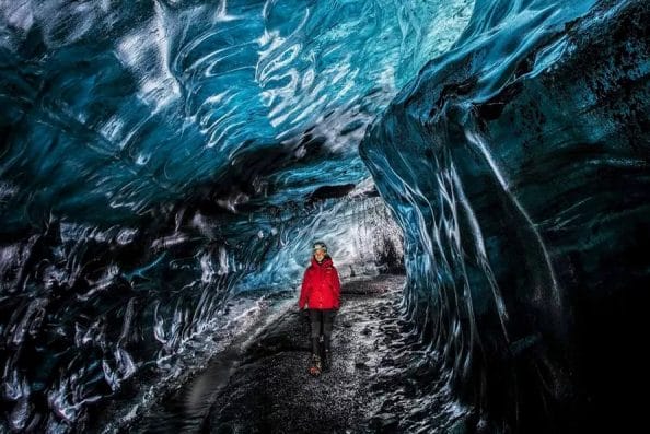 A visitor explores the Crystal Ice Cave, standing still as the light filters through the mesmerizing, icy-blue walls of the glacier.