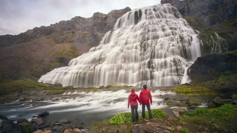 two people standing in front of Dynjandi waterfall in the Westfjords of Iceland