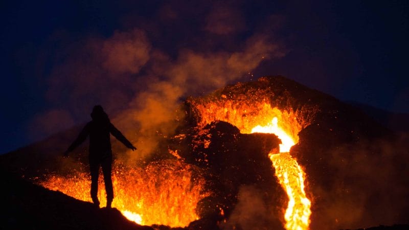active volcano tour, man standing in front of Geldingadalur erupting volcano in Iceland