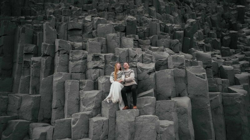 two people sitting in the basalt columns at Reynisfjara black sand beach, Honeymoon in Iceland