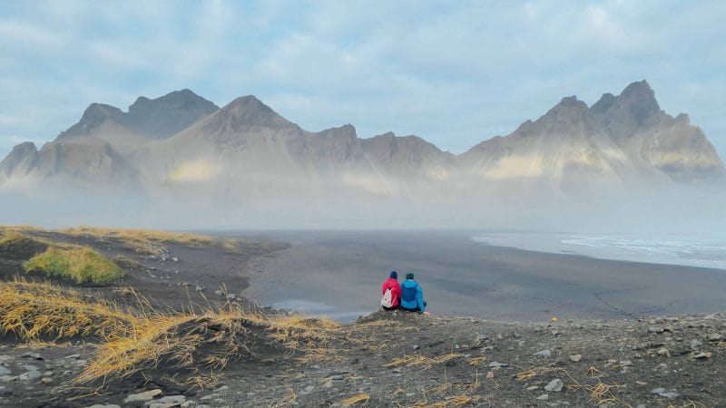 Honeymoon in Iceland, two people sitting in front of Stokksnes in east Iceland