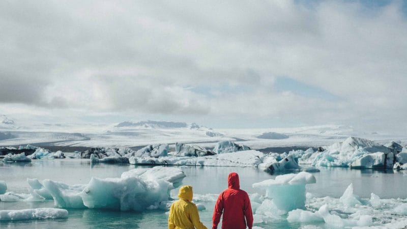 two people standing in front of Jokulsarlon glacier lagoon wearing yellow and red jackets