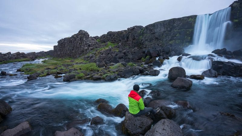 man sitting in front of Öxarárfoss waterfall in Thingvellir National Park in the Golden Circle