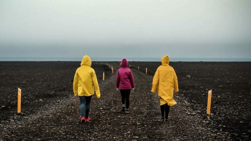 three people in yellow raincoats walking the black sand beach to Solheimasandur Plane Wreck in south Iceland