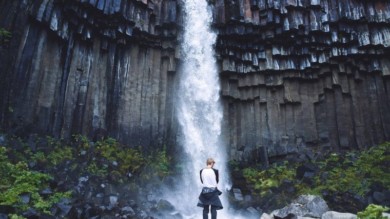 man standing in front of Svartifoss waterfall in Skaftafell Vatnajökull National Park in south Iceland