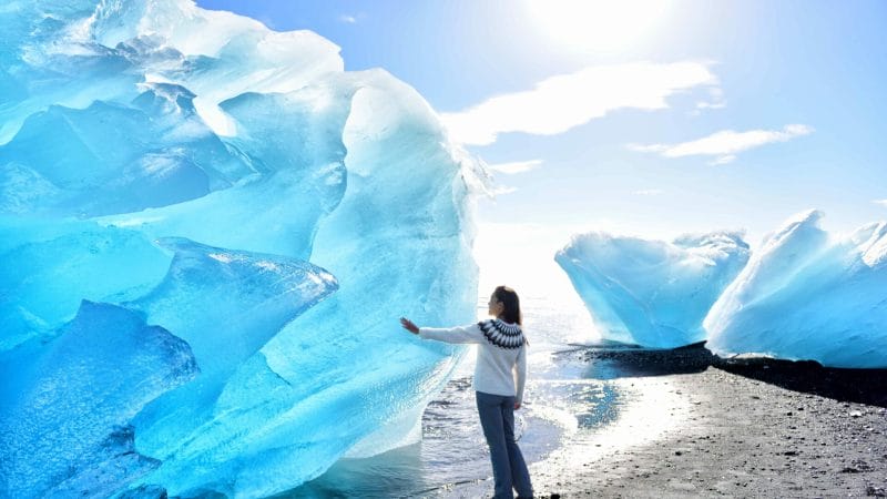girl standing in front of an ice berg at the Diamond beach in South Iceland