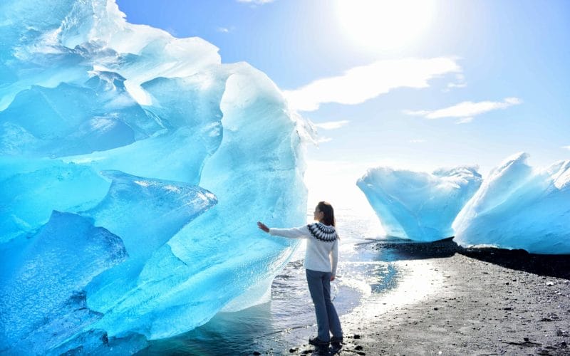 girl standing in front of an ice berg at the Diamond beach in South Iceland