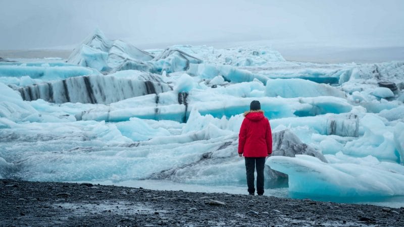 woman in red coat next to Jokulsarlon glacier lagoon in south Iceland