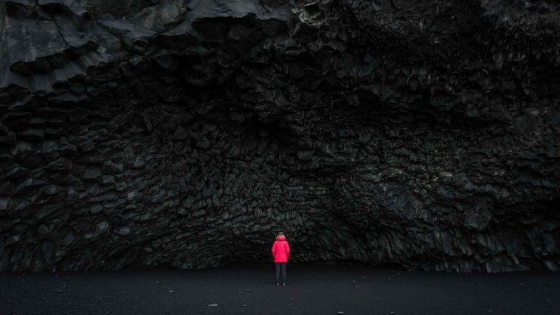 woman in red coat next to the cave at Reynisfjara black sand beach in south Iceland