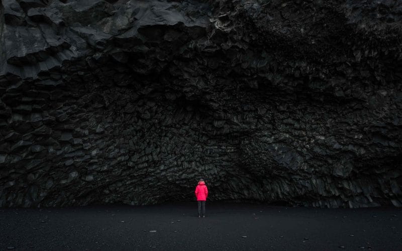 woman in red coat next to the cave at Reynisfjara black sand beach in south Iceland