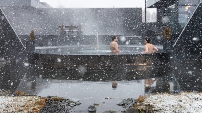 snow falling on two people at Krauma geothermal baths and spa in west Iceland during winter