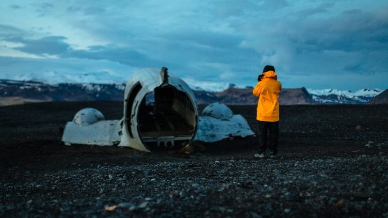 man in yellow raincoat in front of Solheimasandur plane wreck on Solheimasandur black sand beach in south Iceland
