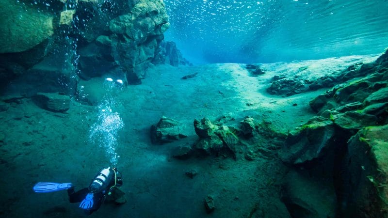 man diving in the clear water in Silfra in Thingvellir National Park in Iceland, man diving between the continents of Europe and North America