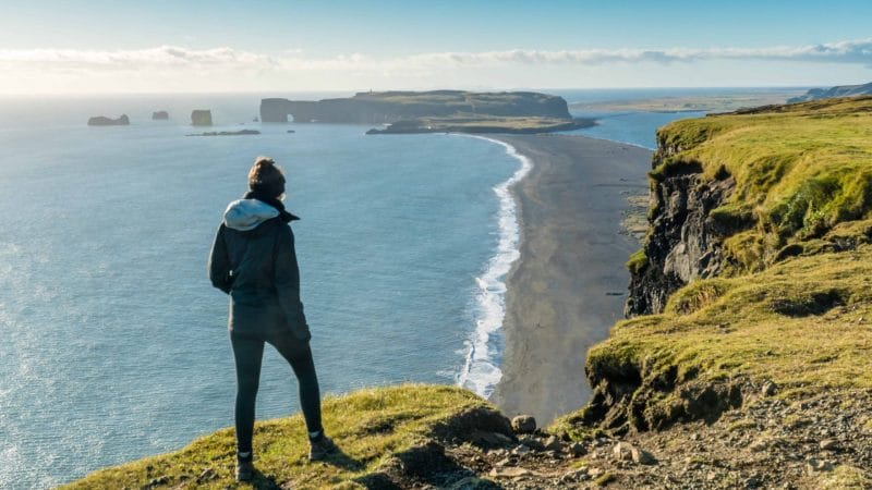 woman standing on top of Reynisfjall watching over Reynisfjara black sand beach and Dyrhólaey